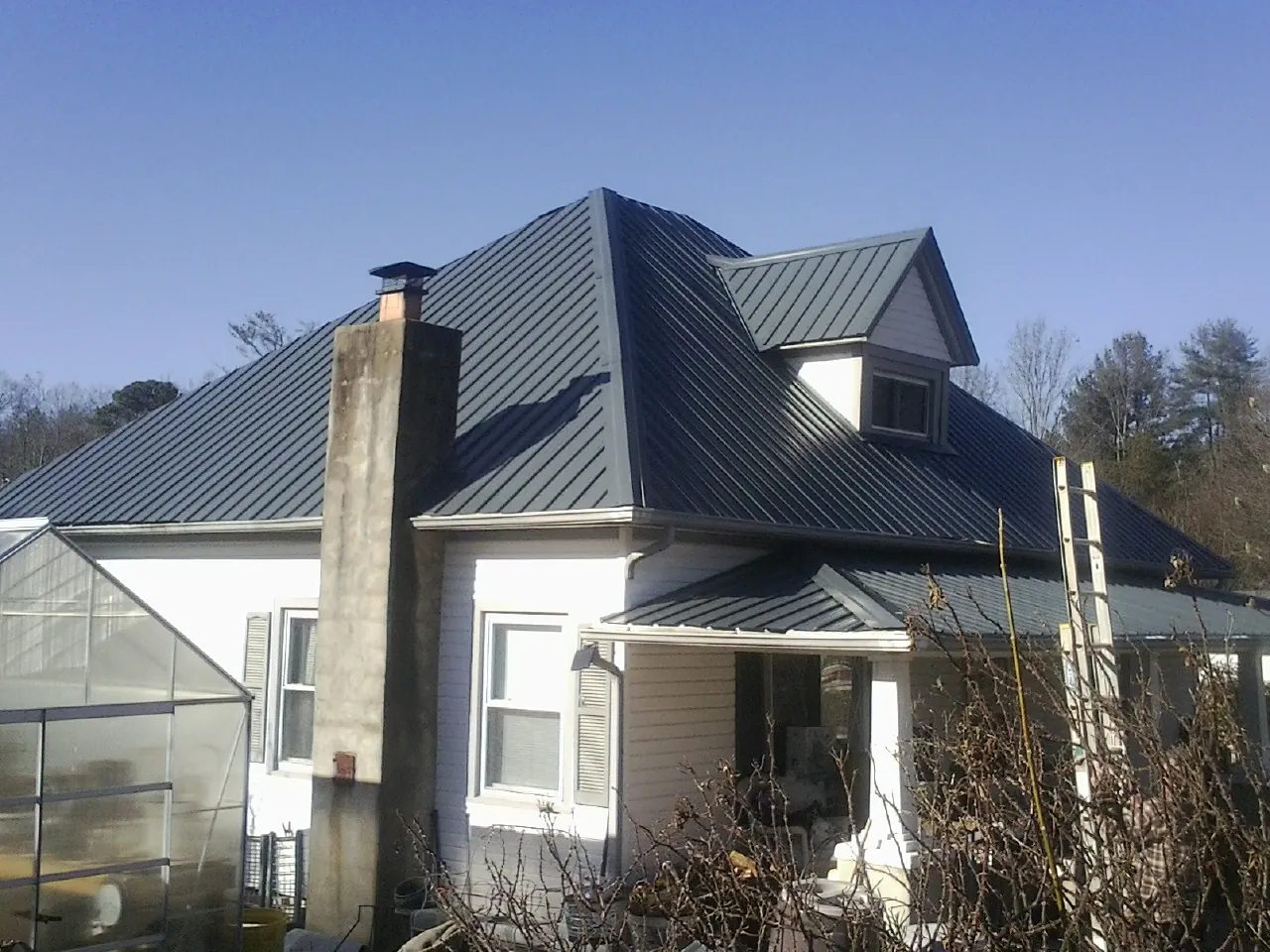 Dark blue standing seam metal roof on a white farmhouse with dormer — Slate & Tile Roof Repair by Roofing Brothers in New Raymer