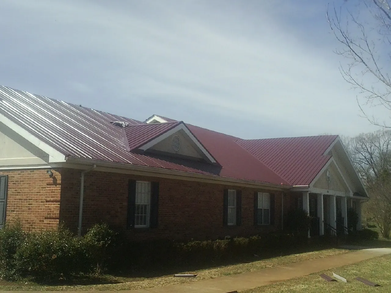 Red metal roof with gabled entries on a long brick building, from a Hail Damage Roof Repair job in New Raymer