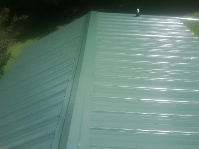 New green metal panels meeting at the ridge of a roof — Flat Roof Repair work by our crew in New Raymer