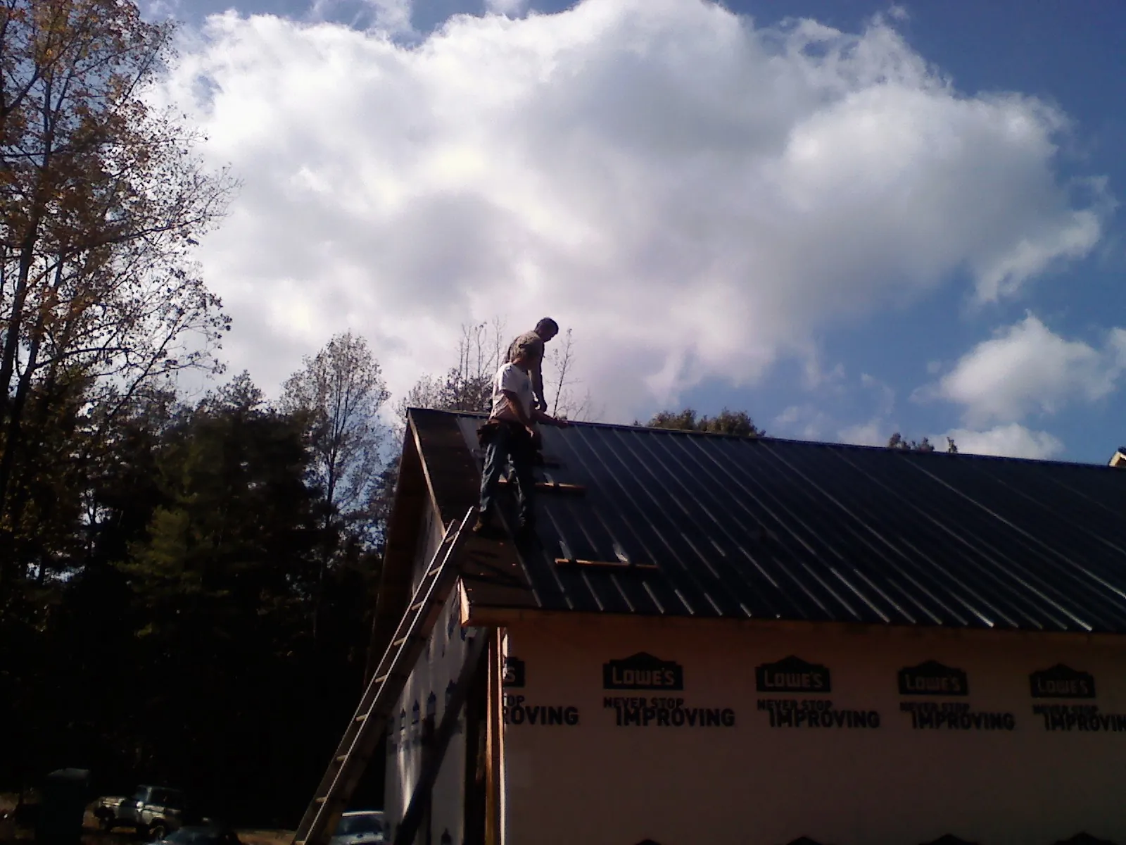 Roofer fastening dark metal panels high against a cloudy sky, from a Roof Inspection job in New Raymer
