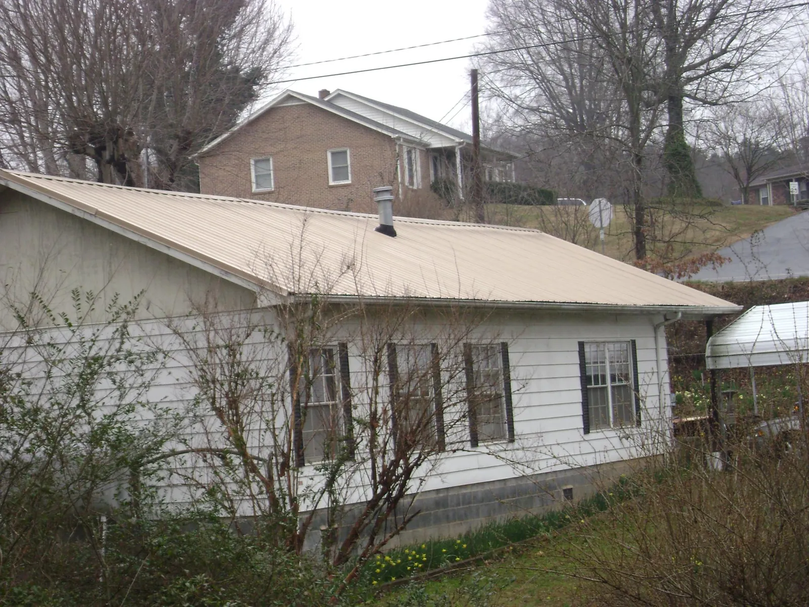 Tan metal roof on a white sided house set into a hillside — Commercial Roofing by Roofing Brothers in New Raymer